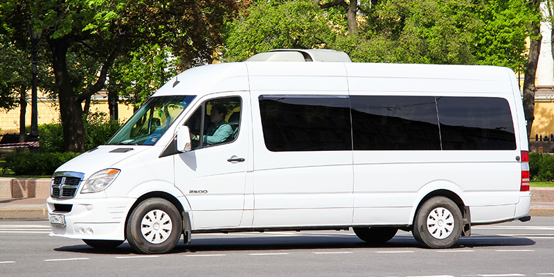 Large White Dodge Sprinter passenger van driving on street Large White Dodge Sprinter passenger van driving on street