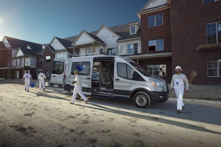 Silver Ford Transit cargo van parked outside construction site with crew